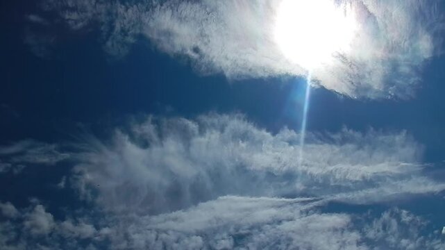 Blue sunny sky, white Cirrus clouds with pearl colors around sun and flying butterflies in summer weather - natural sky background. Topics: cloud iridescence, irisation, optical phenomenon, nature