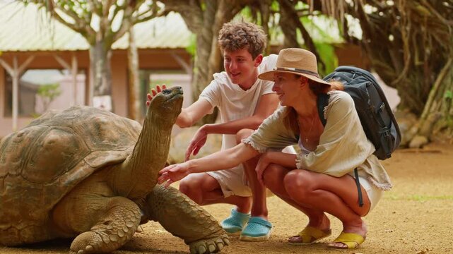 A mother and son pet the head of a rare, giant turtle on the tropical island of Mauritius