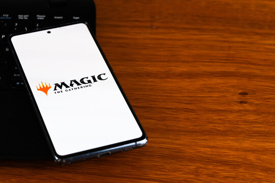 Punta Arenas, Chile &ndash; March 31, 2026: The Magic: The Gathering logo displayed on a smartphone screen resting on a wooden desk next to a laptop keyboard