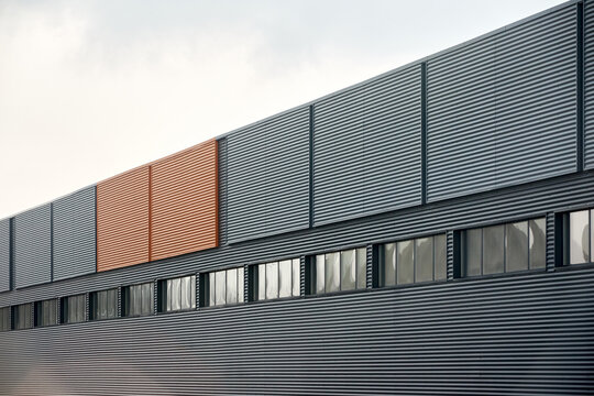 Architectural facade with orange cladding corrugated metal panels, large glass window of industrial or commercial building, contemporary architecture with vertical relief and material contrast.