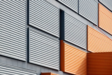 Fototapeta premium Architectural facade with orange cladding corrugated metal panels, large glass window of industrial or commercial building, contemporary architecture with vertical relief and material contrast.