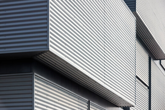 Architectural facade with gray cladding corrugated metal panels of industrial or commercial building, contemporary architecture with vertical relief and material contrast.