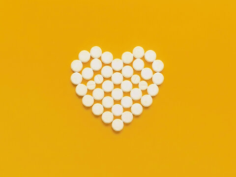 Heart shape made of white pills on yellow background - heart health concept, generative AI