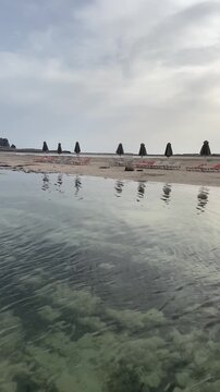 Vertical video of a serene, empty Balos beach. Rows of sunbeds and umbrellas wait on the sand against a backdrop of majestic Cretan mountains and turquoise lagoon waters. High quality 4k footage