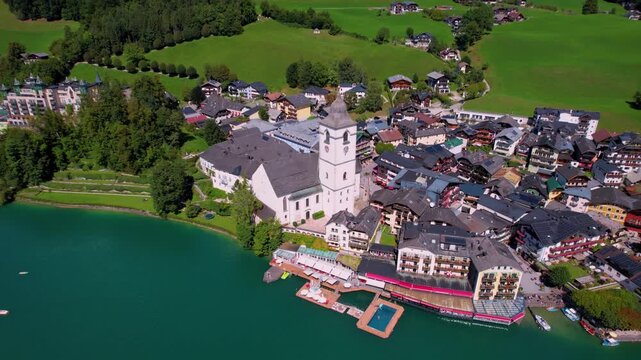 Aerial drone reveal of St Wolfgang village and Pilgrimage Church, white tower above turquoise Wolfgangsee lake, Salzkammergut Austrian Alps, scenic travel destination Austria, reveal shot 4k