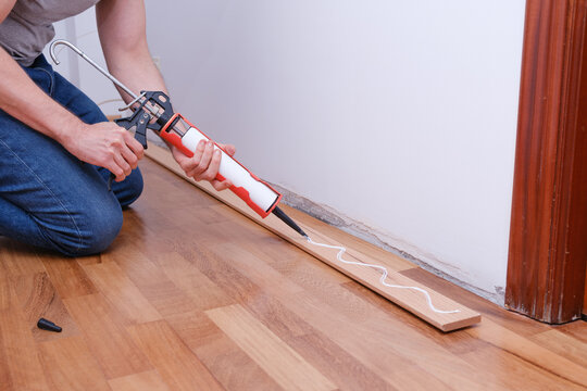 Man applying adhesive with caulking gun for baseboard installation