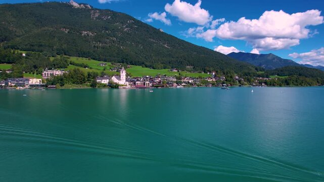 Austria Lake Wolfgangsee aerial 4K. Dynamic drone video flying low over water with fast motorboat crossing towards Saint Wolfgang village. Scenic Alps mountain scenery, Scenic Alpine Lake Life