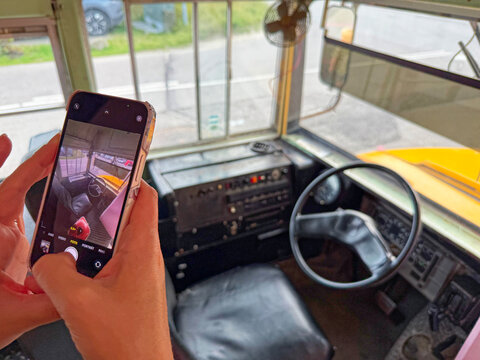 Person taking photo of vintage bus driver seat and steering wheel with smartphone