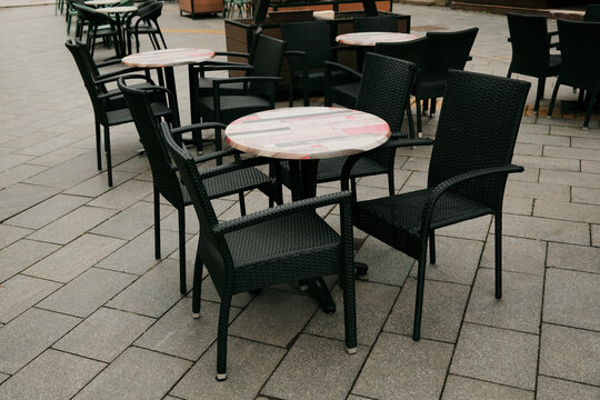 Round tables and chairs of outdoor cafe on paved city street without people. Concept of urban leisure, hospitality, and business environment.