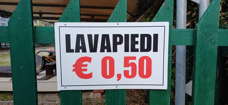 Italienisches Preisschild am Strand: Fu&szlig;w&auml;sche Lavapiedi f&uuml;r 50 Cent an gr&uuml;nem Holzzaun