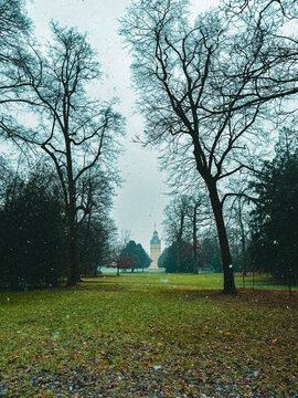Snowfall Serenity in a Historic European Park with a Baroque Palace Tower Framed by Bare Winter Trees