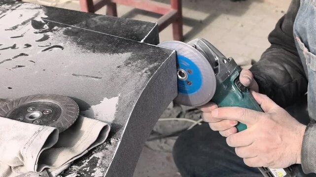 Worker uses tool to shape stone block in workshop during daytime hours