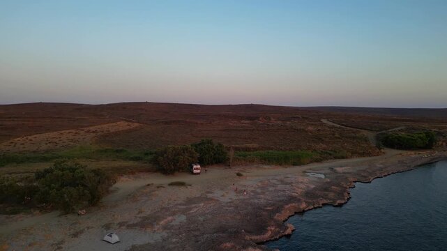 Aerial view of Paralia Skidi beach on Limnos Island, Greece, featuring a parked campervan beside a remote coastline. Clear Mediterranean water and rugged terrain highlight peaceful wild camping