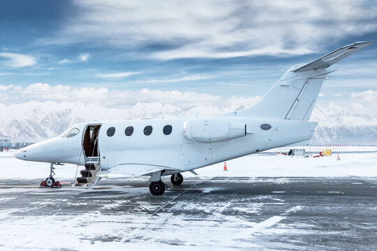 Modern white bizjet with an opened gangway door at the winter airport on the background of high picturesque snow capped mountains