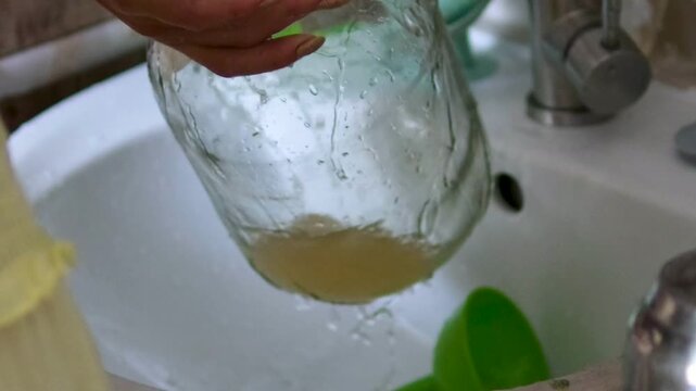 Series shows a woman preparing kombucha in a rural Ukrainian home. She rinses the tea mushroom, cleans jars, pours fermented drink into bottles, highlighting traditional lifestyle and health benefits.