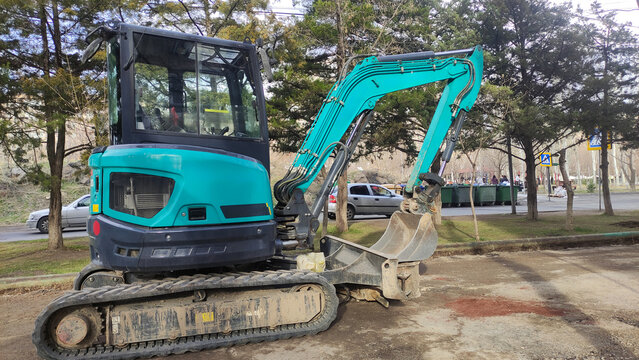 Detailed view of a compact excavator with bucket attachment on a street construction site, emphasizing machinery, urban work, and infrastructure maintenance.