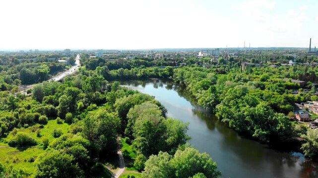 Scenic drone view of the Psel River in Sumy, Ukraine, surrounded by lush greenery and natural landscape. Busy road with moving traffic. Transport bridge over the river with cars driving along it.