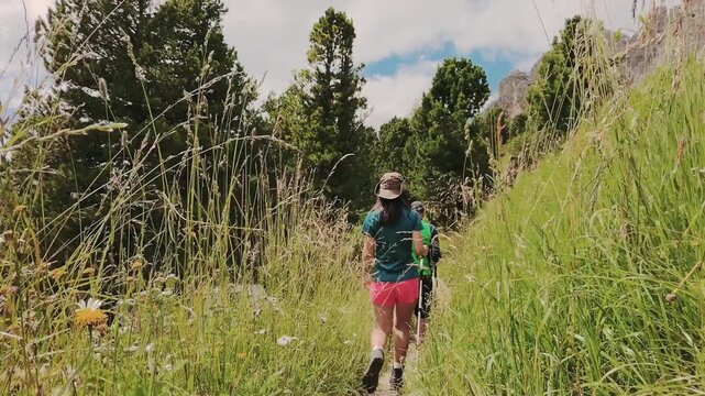 fClose up tracking view couple treks through lush meadows forest in famous summer destination Dolomites. Active lifestyle weekend get away trek in Europe summer holidays