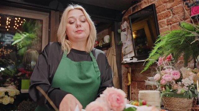 White florist arranging pink roses, boutique hands skillfully trim stems and tie ribbon around romantic bouquet on wooden counter with brick wall backdrop and warm lighting, scissors and twine nearby,