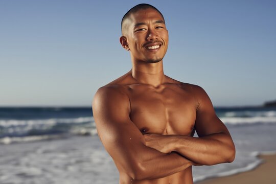 Shirtless man standing with arms crossed on beach shore
