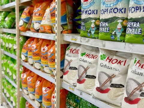 Depok, Indonesia - March 31, 2026: A variety of 5kg rice bags from popular Indonesian brands including Topi Koki, Hoki, and Induk Ayam are stacked on a retail aisle rack at Tip Top Supermarket