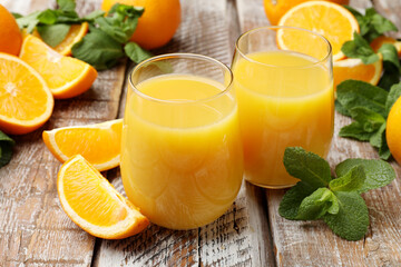 Citrus juice in glasses, fresh oranges and mint leaves on wooden table, closeup © New Africa