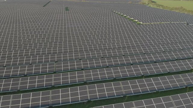 Aerial drone video of a large solar panel field at an energy company facility. Rows of photovoltaic panels capture sunlight to generate clean electricity, representing renewable energy, sustainability
