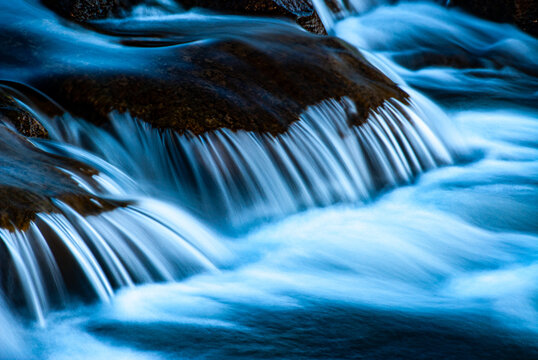 Flowing water over rocks in Iceland with smooth long exposure effect. Peaceful Iceland nature scene with blue tones, soft motion, and detailed texture of river and stones.
