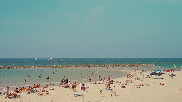 Wide shot of Tel Aviv beach in Israel during summer vacation or weekend. Local people and tourists enjoy hot weather to bathe swim and play in Mediterranean Sea water. Fun on sunny day on sandy beach