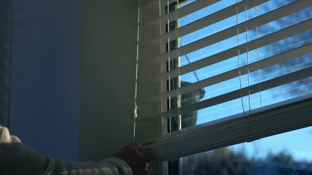 Woman opending venetian blinds window slats string in sunlight 