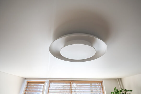 Close-up of a stylish disc-shaped ceiling chandelier on a matte white ceiling. Soft, diffused lighting, clean lines, and a minimalist design create a calm atmosphere.
