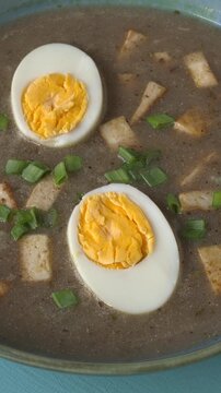 Vegetarian version of sour rye soup with tofu and hard-boiled eggs - blue background, vertical video.