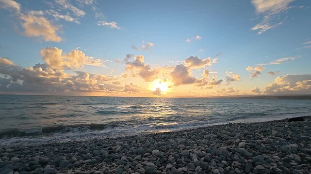Dramatic sunset over pebble beach with stormy sea and cloudy sky in Akrotiri, Cyprus