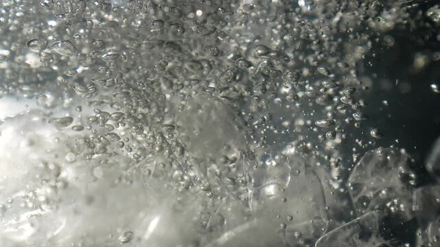 Ice cubes falling into water with oxygen bubbles, frost patterns, and soft light reflections. Concepts for beauty advertising, menu designs for bars and restaurants, cryotherapy.