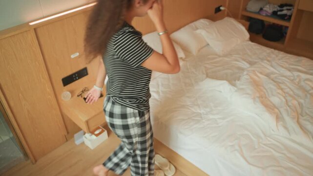 Woman collapsing onto hotel bed exhausted, walks into room, removes shoes, flops face down across rumpled sheets, arms spread, sighs, LED mood lighting, bedside table with phone and tissue box, moment