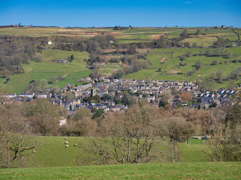 Wide view of Pateley Bridge in Yorkshire UK, with stone houses set among green fields and rolling hills under a clear blue sky