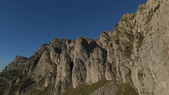 Stunning Golden Hour Drone View under rocky Bucegi Coltii Tapului cliffs, powerful contrast side lighting, dynamic backward flight with perpendicular pull out reveal for copious copy space graded 4K