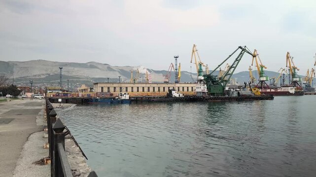 Industrial panorama of commercial sea port in Novorossiysk Tsemes Bay with massive harbor cranes cargo ships and grain elevator conveyor system at Black Sea coast during daytime authentic wide shot
