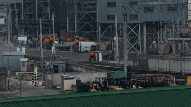Orange industrial terminal tractor driving through Novorossiysk sea port logistics hub stopping at security barrier gate then moving forward captured with 200mm telephoto lens authentic shot