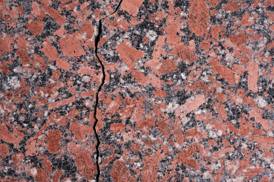 Polished natural stone surface or granite slab with red, grey, white, and black mineral patterns. The crack running across the background.