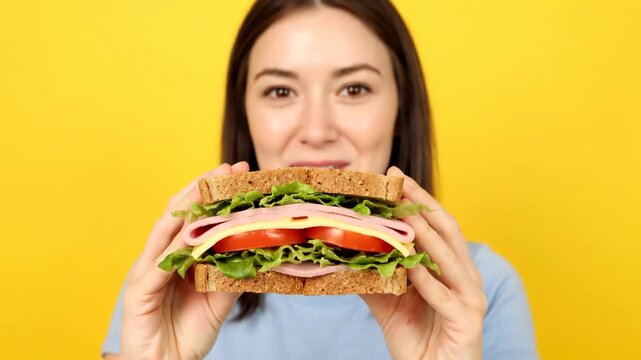 Happy young caucasian woman smiling while holding a big fresh sandwich. Hungry female preparing to eat a delicious ham and cheese sub for a quick lunch