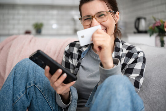Young Woman Shopping Online With A Smartphone While Laughing And Holding A Paying Card