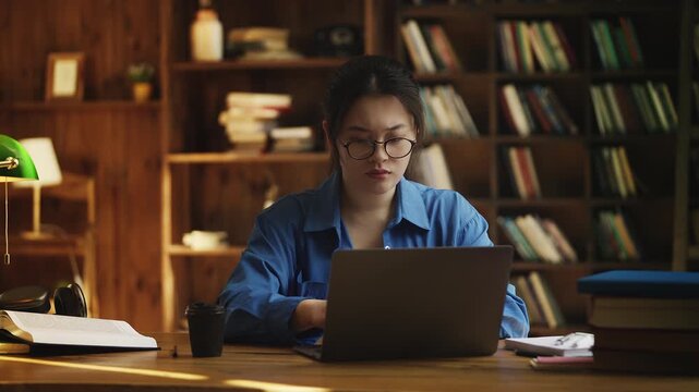 Young Asian woman works on laptop in a library, faces problems with computer