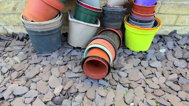 Closeup tilt shot of empty plastic nursery grow plant pots of various colors and sizes, stacked outside against a brick wall in a garden or yard.