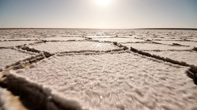 Low angle view of a dry salt flat landscape under a bright sun with cracking patterns and textures