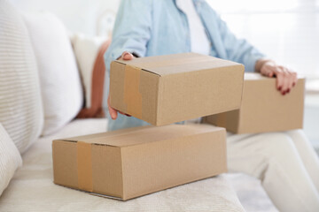 Fototapeta premium Parcel delivery. Woman with cardboard boxes on sofa at home, closeup