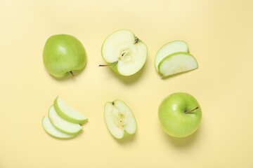 Whole and cut fresh apples on pale yellow background, flat lay