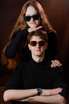 Cool siblings or friends in dark outfits with sunglasses against brown background.