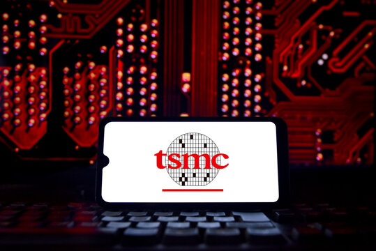 TSMC (Taiwan Semiconductor Manufacturing Company) logo on a smartphone screen with semiconductors in the background. The world's largest third-party semiconductor manufacturer.