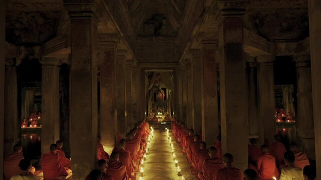 Group of Buddhist monks praying in a row with candlelight inside a historic Khmer temple in Cambodia